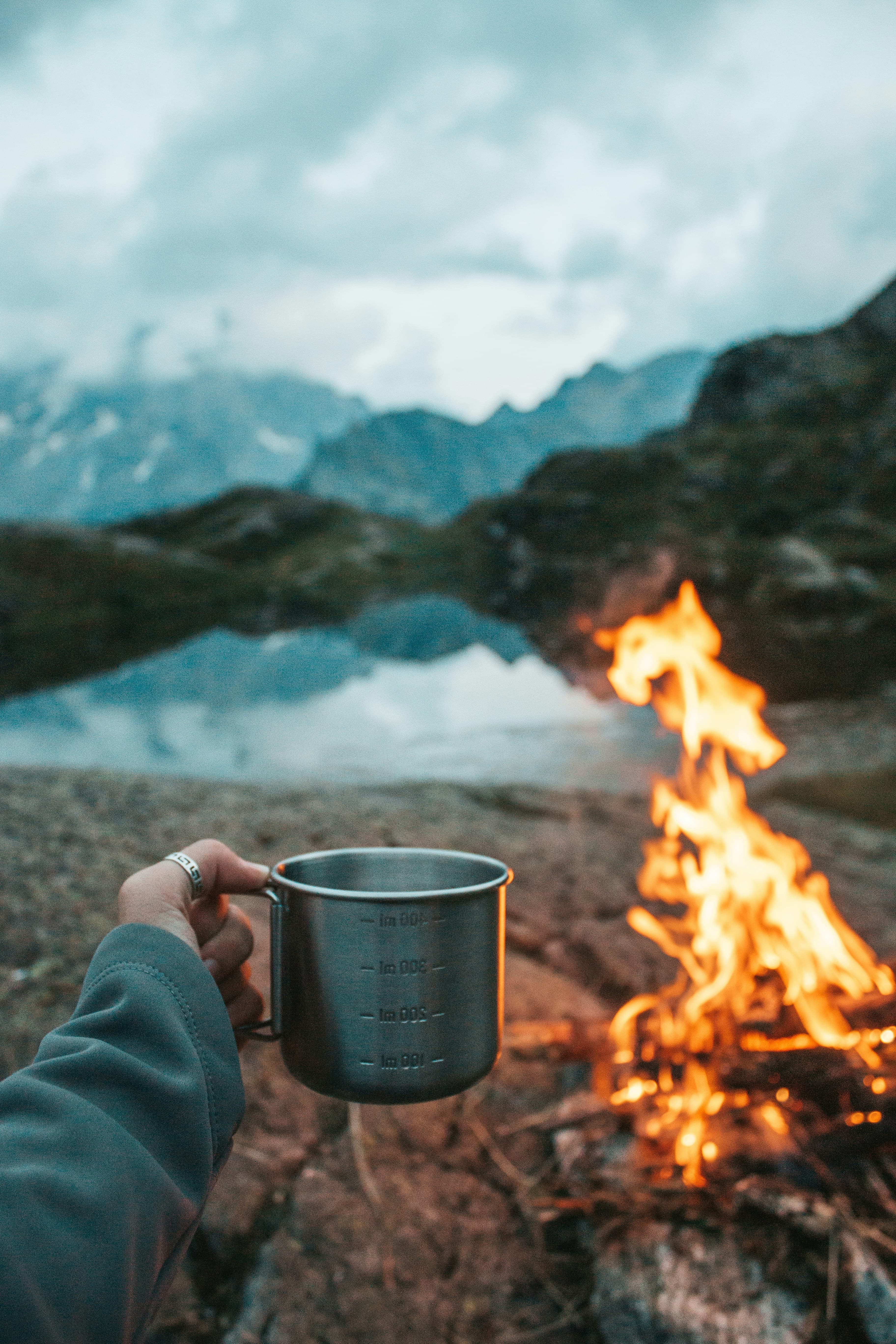 Camping mug by campfire with mountain lake in background